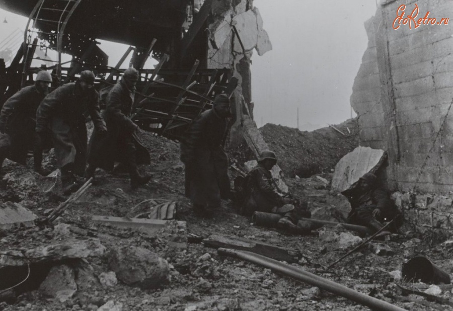 Волгоград - Четверо советских пленных проходят по разрушенному сталинградскому заводу мимо двух немецких солдат.